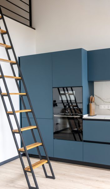Matte blue cabinetry with marble back splash and a ladder to the mezzanine, reflections in the glossy oven create depth and a trendy loft mood.